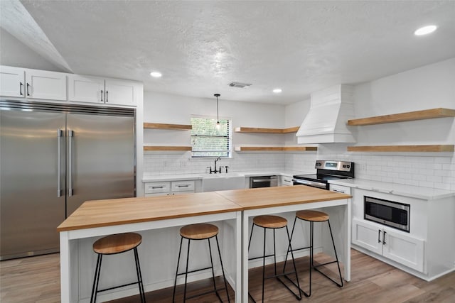 kitchen featuring a sink, wooden counters, appliances with stainless steel finishes, custom exhaust hood, and open shelves