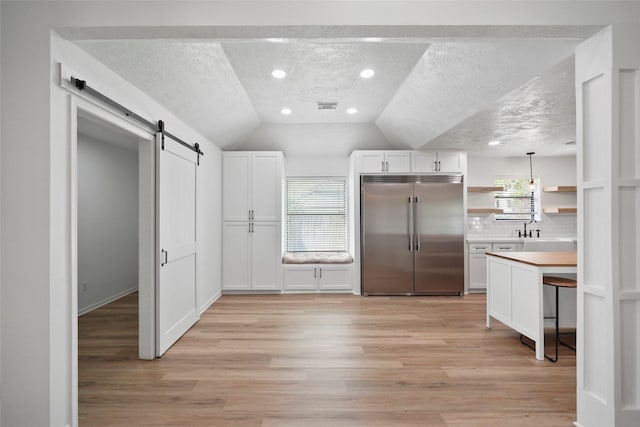 kitchen featuring open shelves, visible vents, light wood-style flooring, a barn door, and built in refrigerator