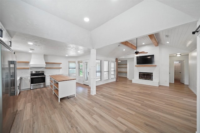 kitchen featuring lofted ceiling with beams, stainless steel appliances, premium range hood, butcher block counters, and open shelves