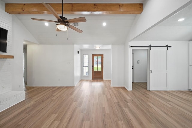 unfurnished living room featuring light wood-style floors, beamed ceiling, baseboards, and a barn door