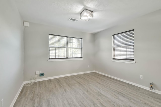 empty room featuring plenty of natural light, visible vents, baseboards, and wood finished floors