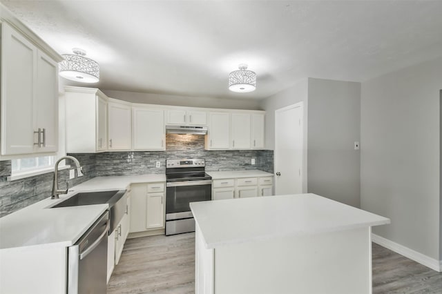 kitchen with under cabinet range hood, stainless steel appliances, a sink, decorative backsplash, and light wood finished floors