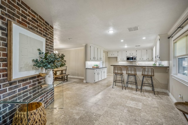 kitchen featuring ornamental molding, stainless steel microwave, a peninsula, and brick wall