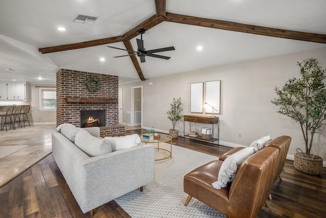 living area featuring baseboards, visible vents, lofted ceiling with beams, hardwood / wood-style flooring, and a brick fireplace