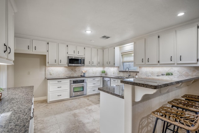 kitchen featuring stainless steel appliances, a peninsula, a sink, visible vents, and dark stone countertops