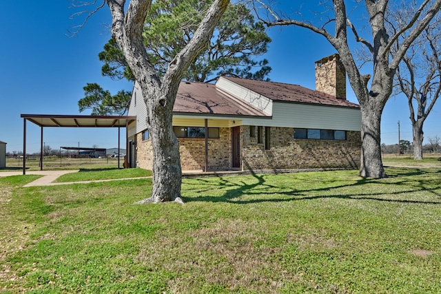 view of front of home with brick siding, a chimney, metal roof, an attached carport, and a front lawn