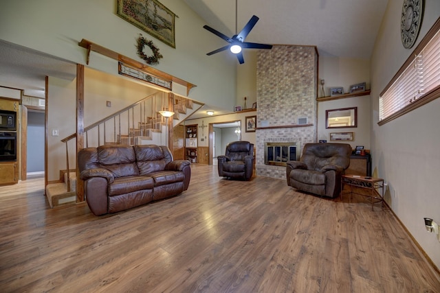 living area featuring a ceiling fan, a towering ceiling, stairway, wood finished floors, and a fireplace
