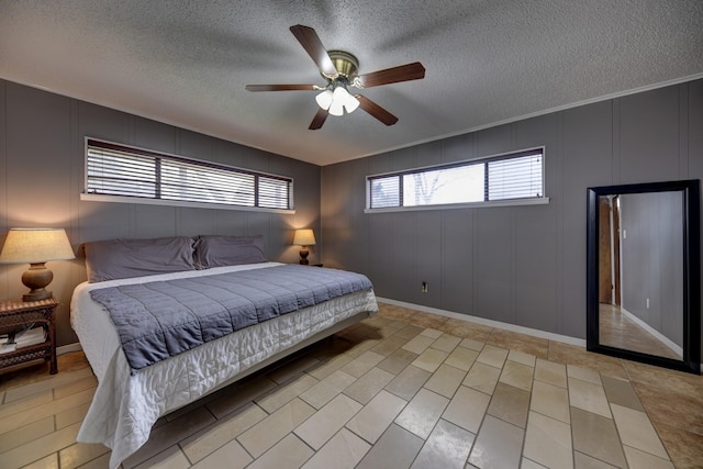 bedroom featuring a ceiling fan, a decorative wall, a textured ceiling, and baseboards