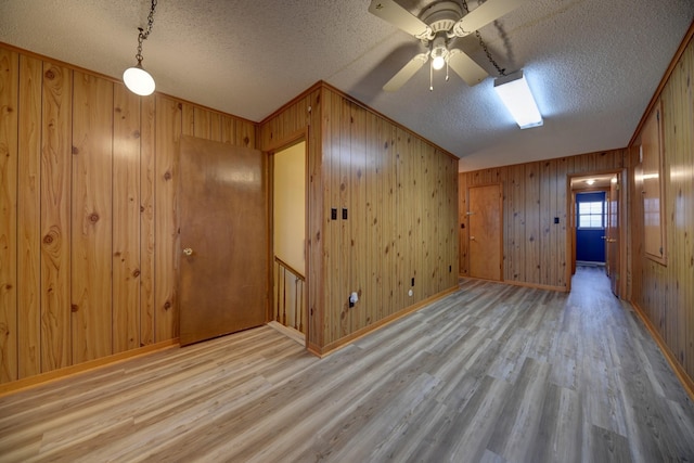 empty room with a textured ceiling, ceiling fan, wooden walls, wood finished floors, and baseboards