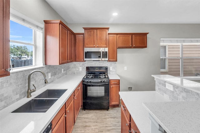 kitchen featuring black gas range, a sink, brown cabinetry, tasteful backsplash, and stainless steel microwave