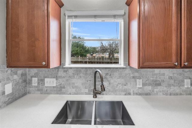 kitchen featuring brown cabinets, decorative backsplash, light countertops, and a sink