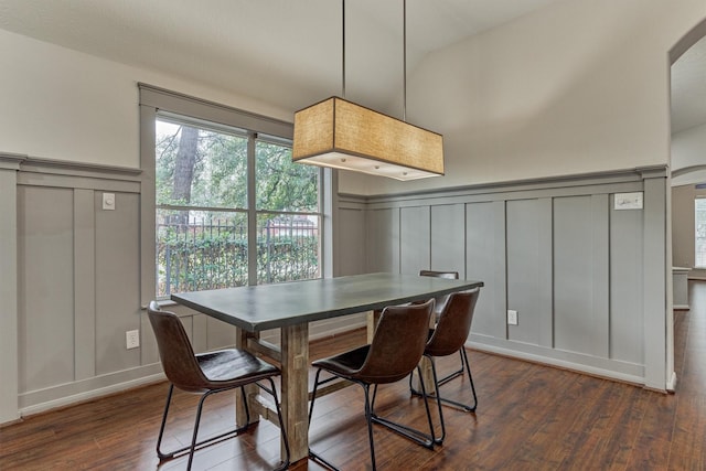 dining area with arched walkways, a decorative wall, and dark wood-type flooring