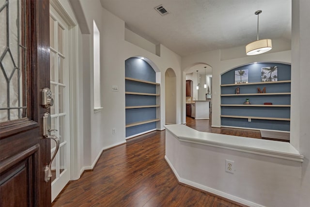 interior space featuring baseboards, visible vents, arched walkways, and dark wood-type flooring