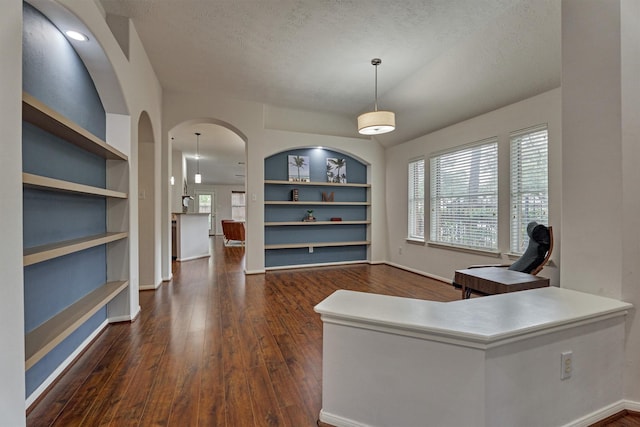 home office featuring plenty of natural light, built in shelves, dark wood finished floors, and a textured ceiling