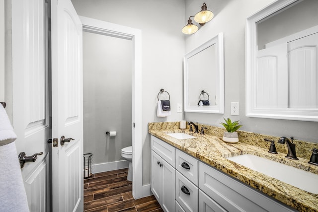 bathroom featuring toilet, wood tiled floor, double vanity, and a sink