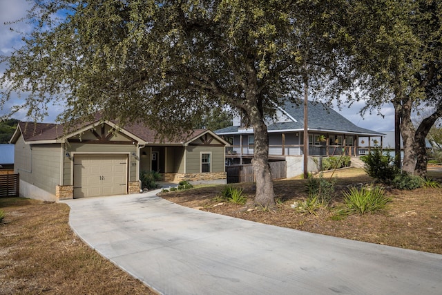 view of front of property featuring a garage, stone siding, driveway, and fence