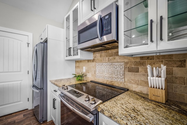 kitchen featuring white cabinets, glass insert cabinets, light stone counters, stainless steel appliances, and backsplash