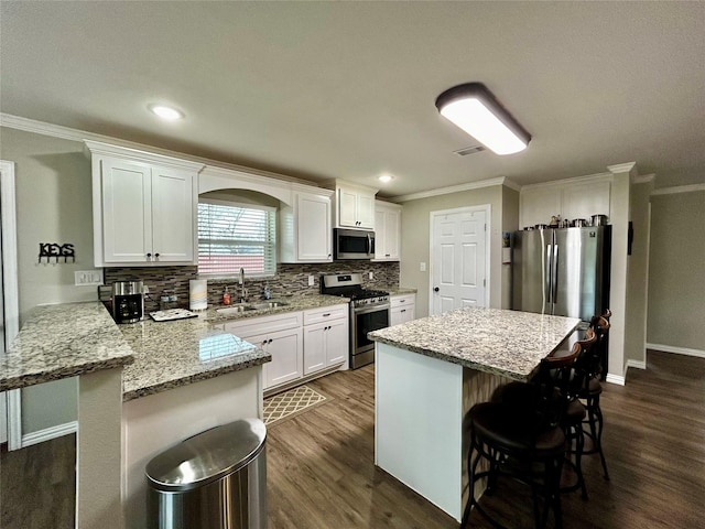 kitchen with a sink, white cabinets, appliances with stainless steel finishes, a kitchen bar, and crown molding