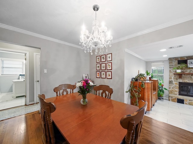 dining area with ornamental molding, visible vents, a stone fireplace, and wood finished floors