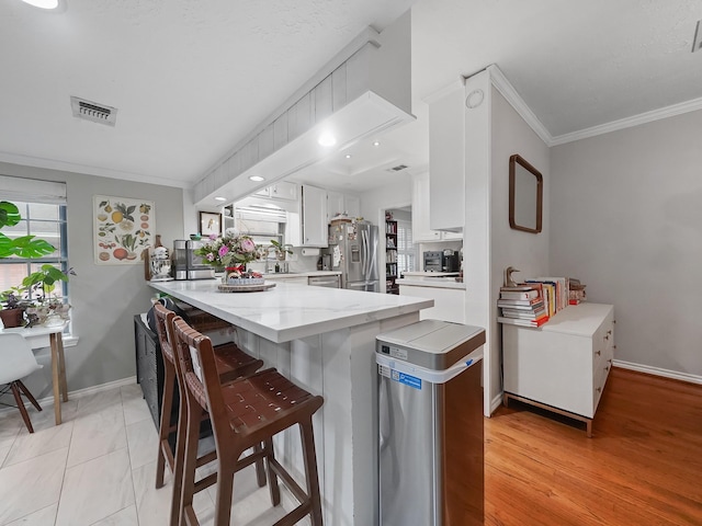 kitchen with a breakfast bar area, ornamental molding, a peninsula, stainless steel appliances, and white cabinetry