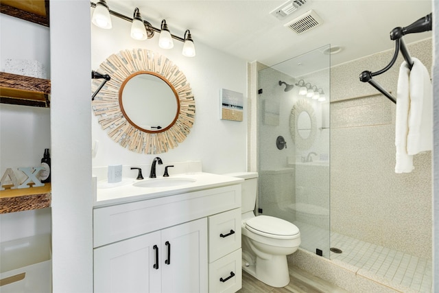 bathroom with visible vents, toilet, vanity, wood finished floors, and walk in shower