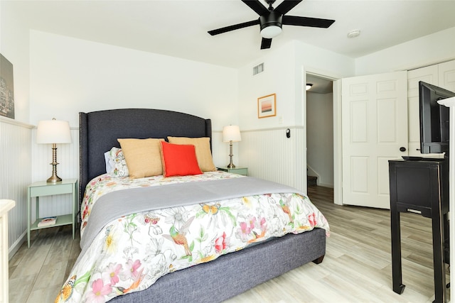 bedroom with a wainscoted wall, wood finished floors, visible vents, and a ceiling fan