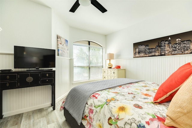 bedroom with ceiling fan, wood finished floors, and wainscoting