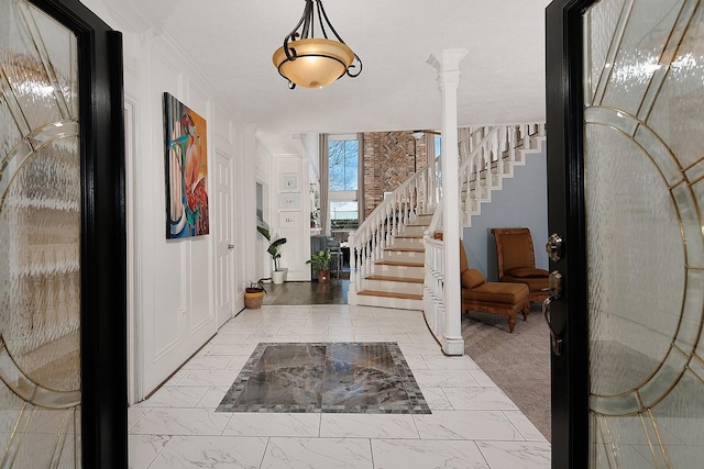 foyer entrance featuring marble finish floor, stairway, crown molding, and ornate columns