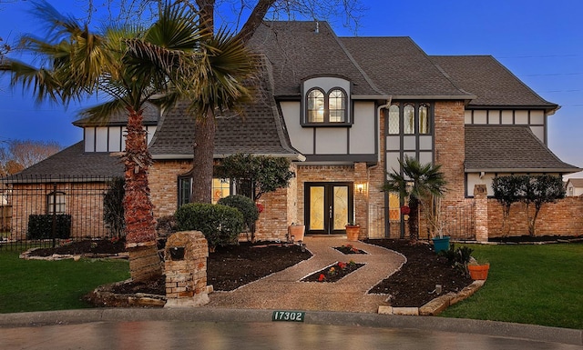 view of front of house featuring brick siding, french doors, roof with shingles, stucco siding, and a front yard