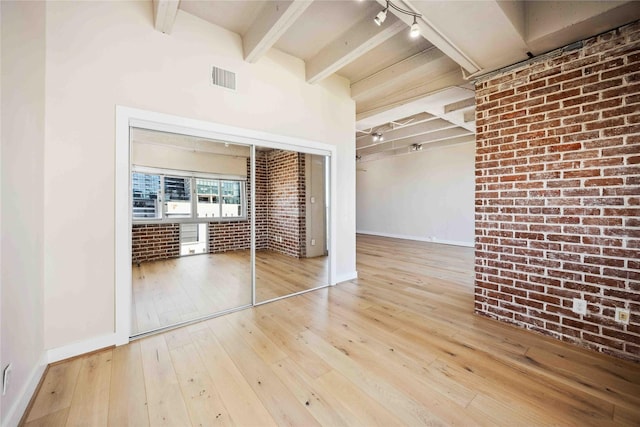 unfurnished bedroom with beam ceiling, a closet, visible vents, brick wall, and hardwood / wood-style flooring