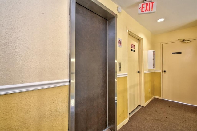 hallway featuring carpet floors, elevator, and a textured wall