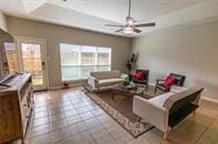 living room with tile patterned flooring, baseboards, a raised ceiling, and a ceiling fan