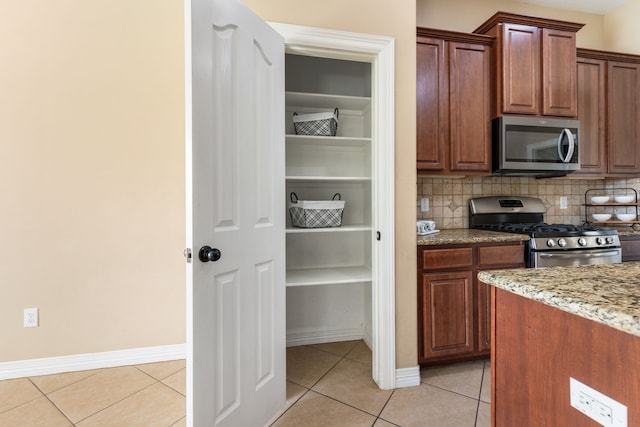 kitchen featuring baseboards, light tile patterned floors, decorative backsplash, light stone counters, and stainless steel appliances