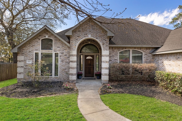 view of front of house featuring fence, brick siding, a front lawn, and a shingled roof