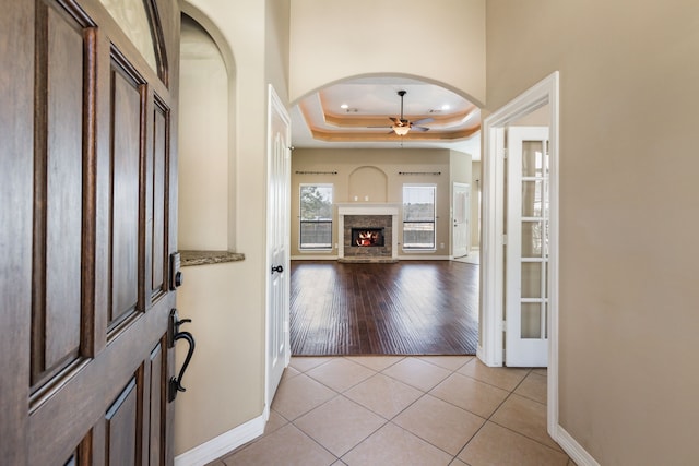 entryway featuring a ceiling fan, arched walkways, a lit fireplace, light tile patterned floors, and a raised ceiling