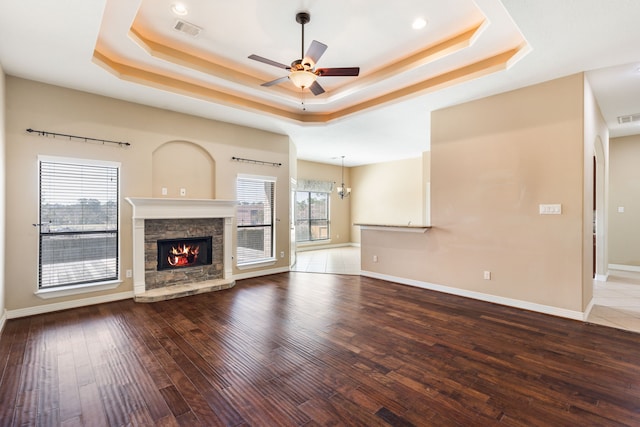 unfurnished living room featuring a ceiling fan, wood finished floors, visible vents, a tray ceiling, and a fireplace