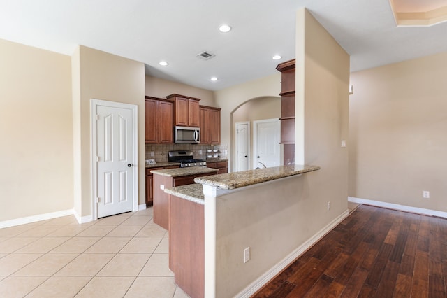 kitchen featuring open shelves, light stone counters, backsplash, appliances with stainless steel finishes, and a peninsula