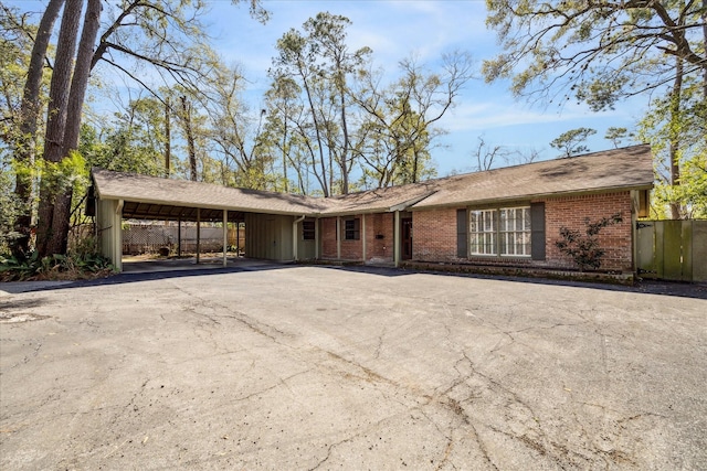 ranch-style house with aphalt driveway, an attached carport, brick siding, and fence