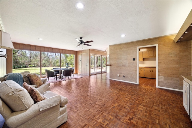 living room with a textured ceiling, recessed lighting, wooden walls, a ceiling fan, and baseboards