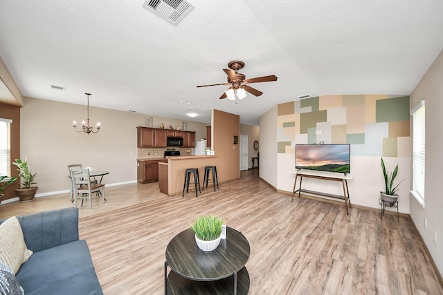 living room with lofted ceiling, light wood-style flooring, ceiling fan with notable chandelier, visible vents, and baseboards