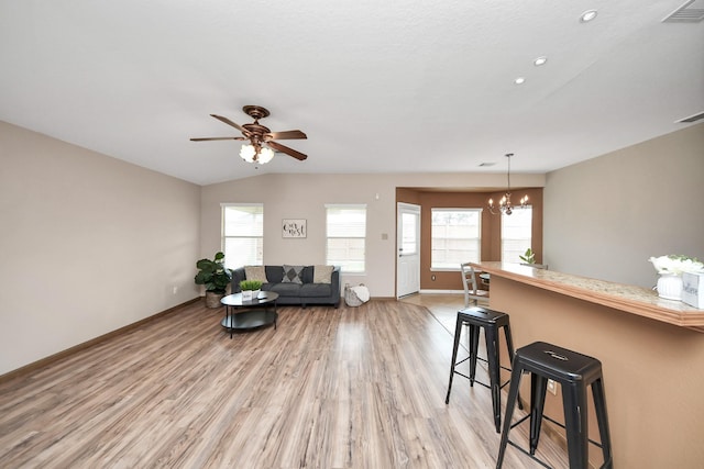 living area with ceiling fan with notable chandelier, light wood-type flooring, visible vents, and baseboards