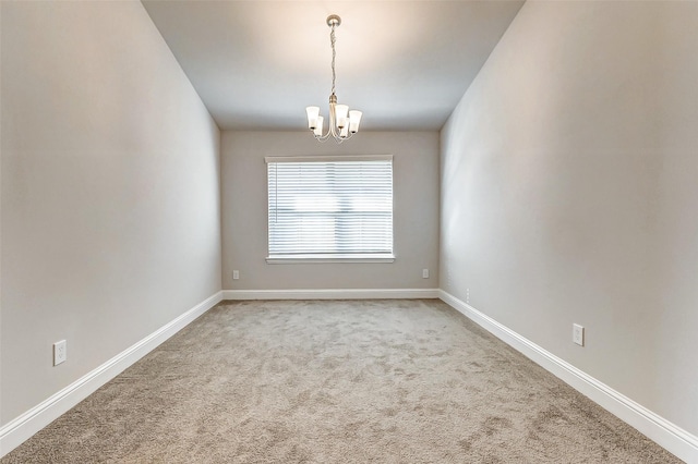 spare room with a chandelier, carpet flooring, and baseboards