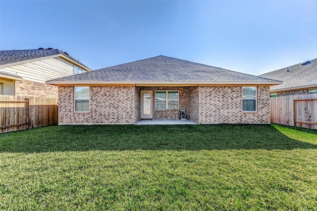 back of house featuring a shingled roof, a fenced backyard, a lawn, and brick siding