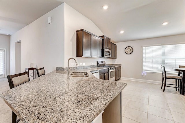 kitchen with appliances with stainless steel finishes, a peninsula, light stone countertops, dark brown cabinets, and a sink