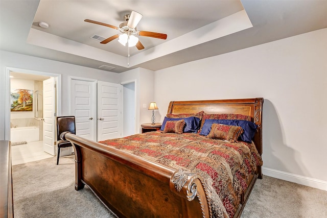 bedroom with a tray ceiling, light colored carpet, visible vents, ensuite bath, and baseboards