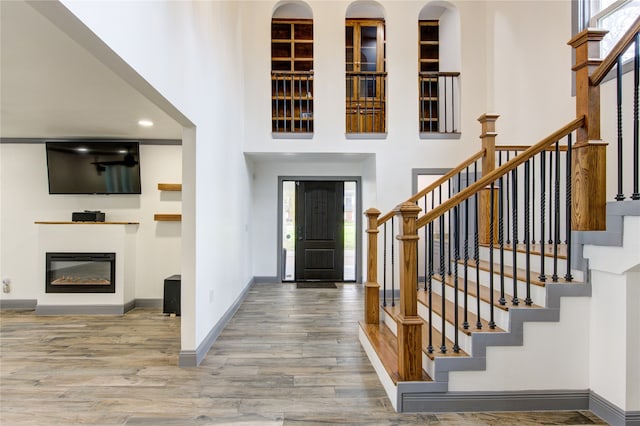 foyer with baseboards, a glass covered fireplace, stairway, wood finished floors, and a high ceiling