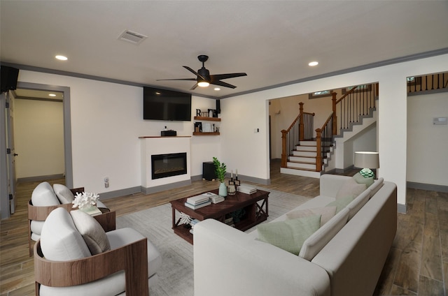 living room with a glass covered fireplace, wood finished floors, visible vents, and stairs