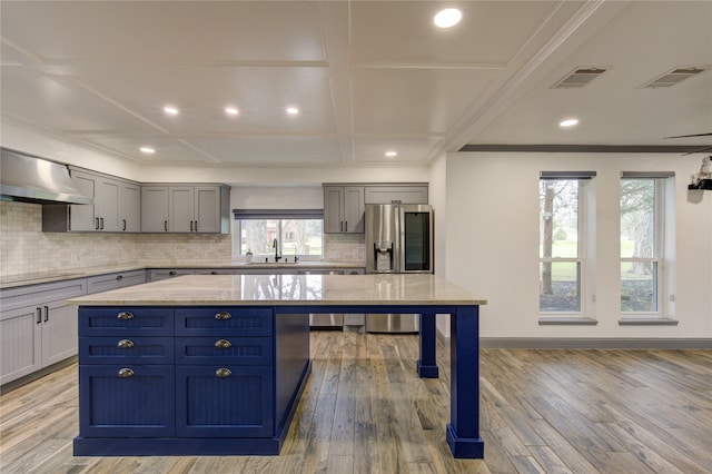 kitchen with wall chimney range hood, stainless steel fridge, a center island, and light wood-style floors