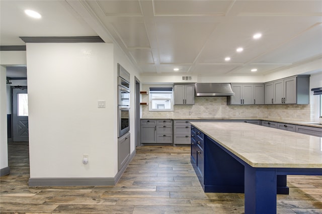 kitchen featuring wood finished floors, wall chimney range hood, gray cabinets, a center island, and tasteful backsplash