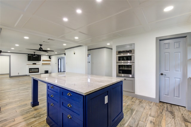 kitchen featuring stainless steel double oven, blue cabinets, a center island, light wood finished floors, and a glass covered fireplace